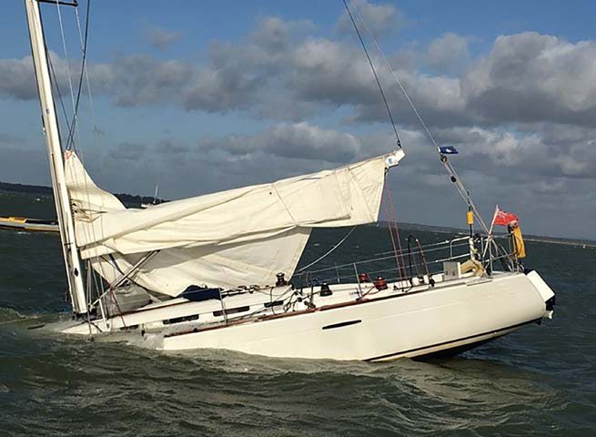 Eine Segelyacht liegt stark auf der Seite, das Vorsegel schlägt lose, im Hintergrund treibt eine rote Tonne.