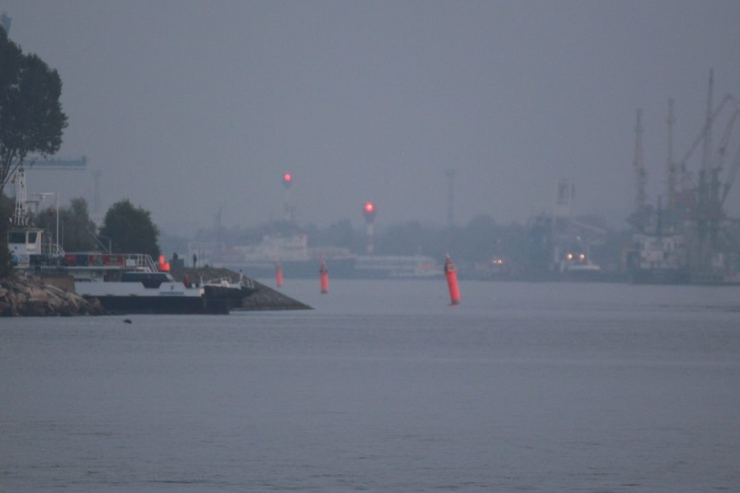 Foto: Richtfeuer mit zwei roten Feuern in der Dämmerung, links oben das höhere Oberfeuer, rechts darunter das Unterfeuer, davor rote Fahrwassertonnen